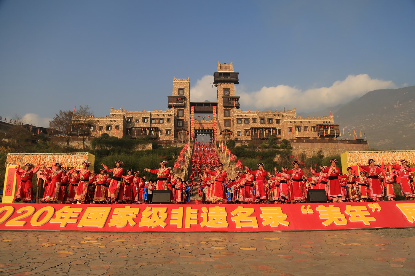 茂县中国古羌城前，非遗传承人身着羌族传统服饰展演「羌年」祭典，条幅标注2020年国家级非遗名录